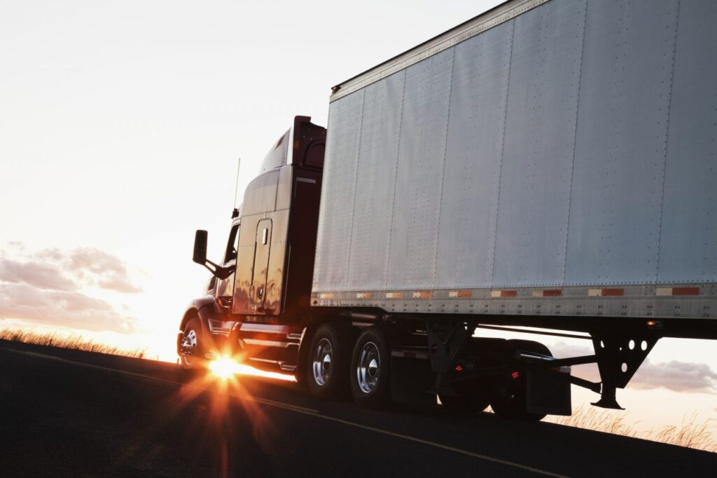 silhouette-of-a-commercial-truck-driving-on-a-highway-at-sunset-